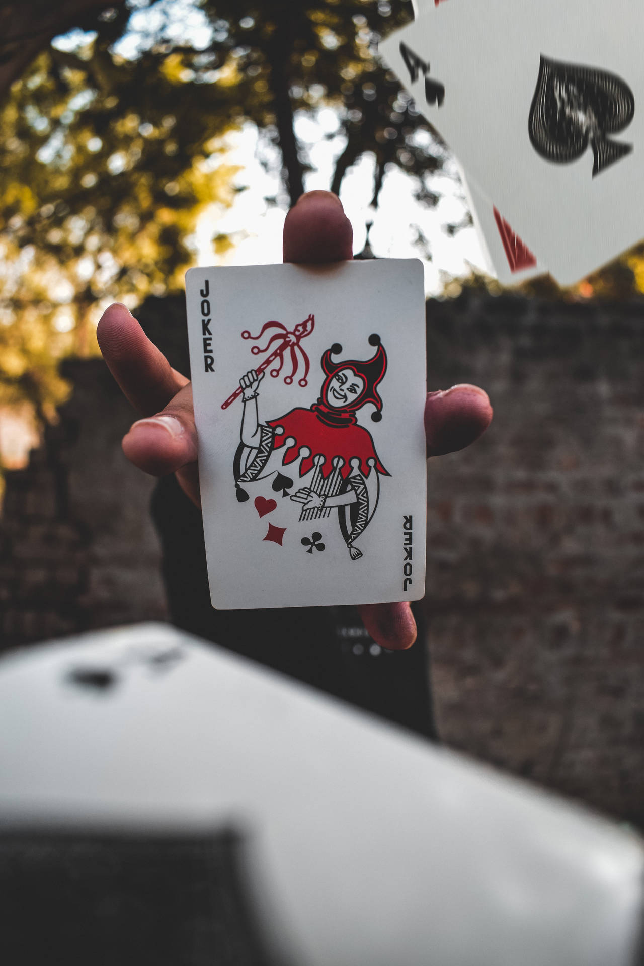 ایک شخص جوکر کارڈ پکڑے ہوئے، دھندلے پس منظر میں کارڈ پھینکتے ہوئے